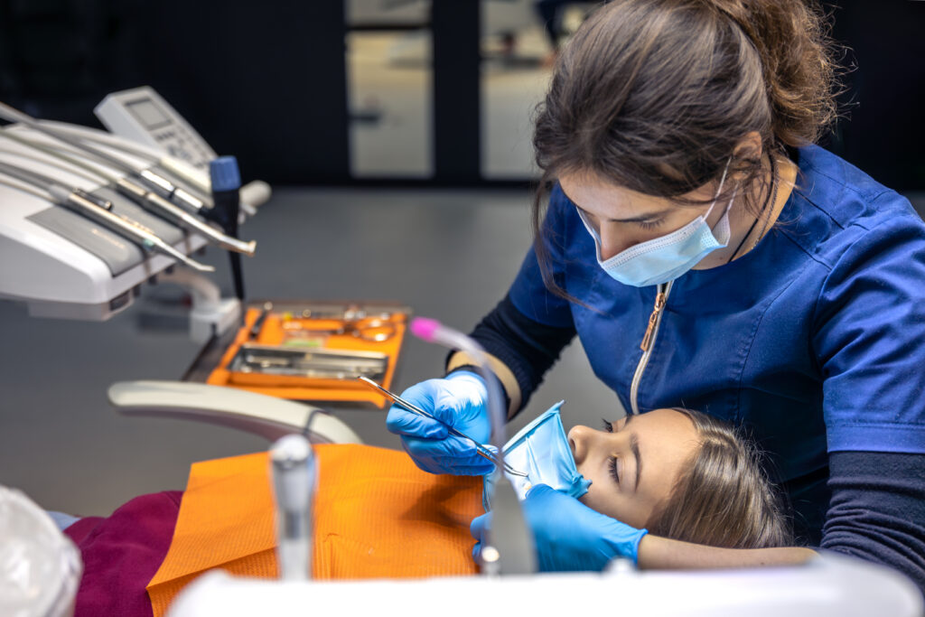 The dentist treats the child's tooth using a rubber dam. Close-up of tooth treatment.