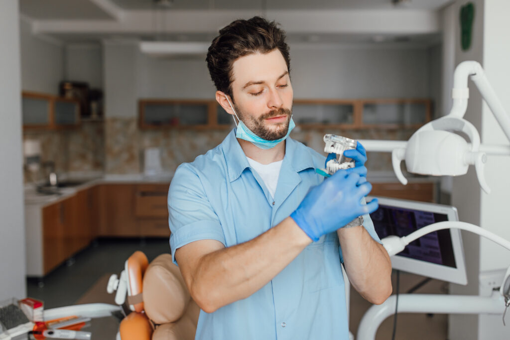 handsome-young-dentist-white-coat-is-holding-plastic-layot-while-standing-his-office