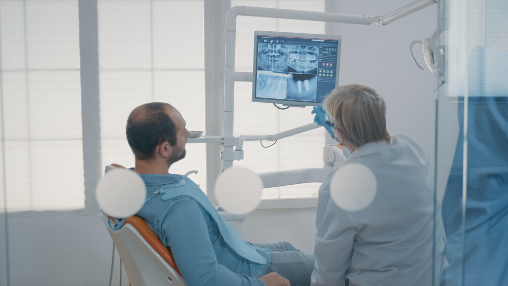 Mature dentist pointing at teeth radiography on monitor