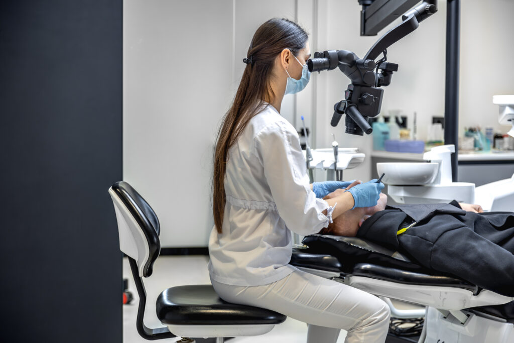 Young female dentist treating patient's teeth with dental microscope. Dentistry concept.